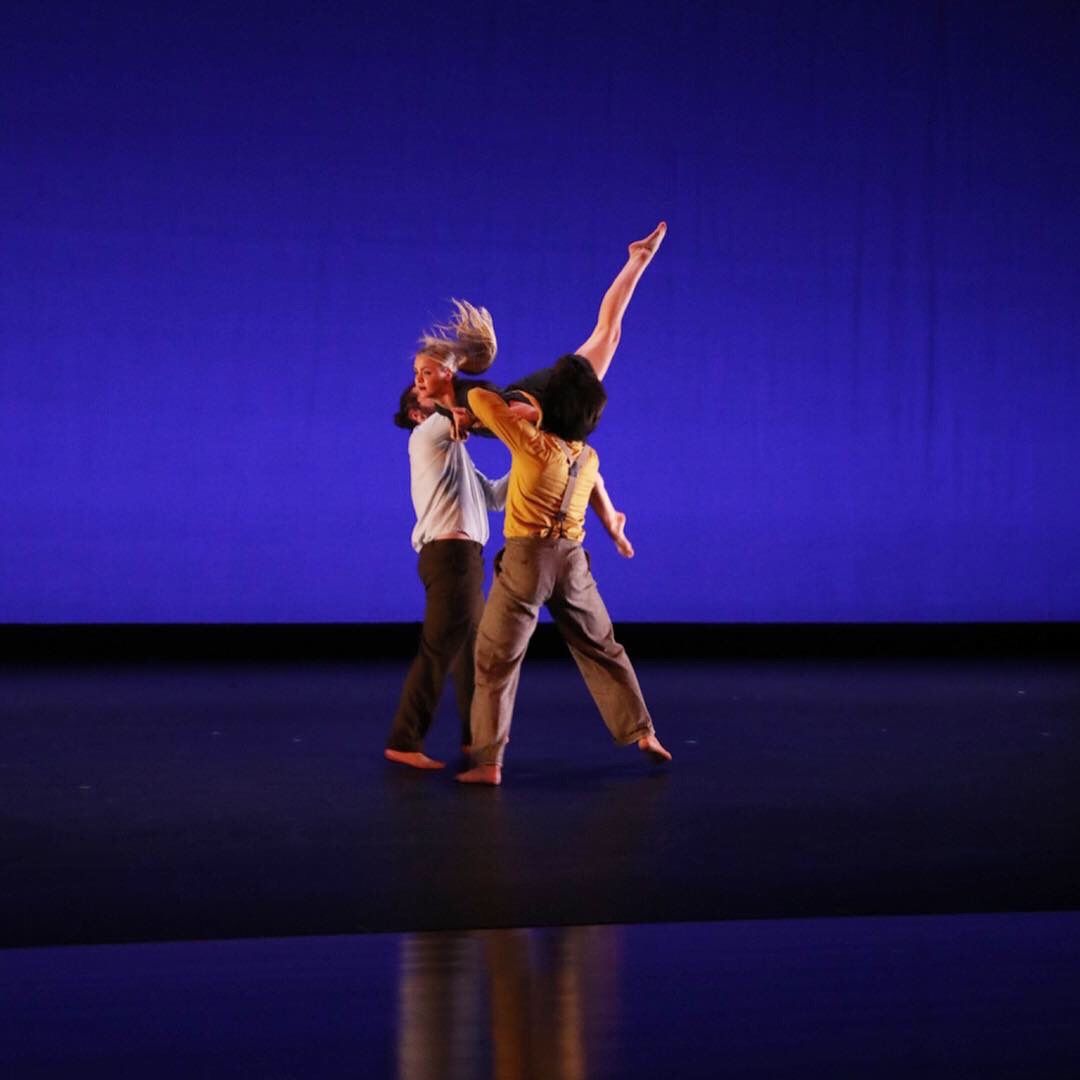 Two men lifting a woman in dance.