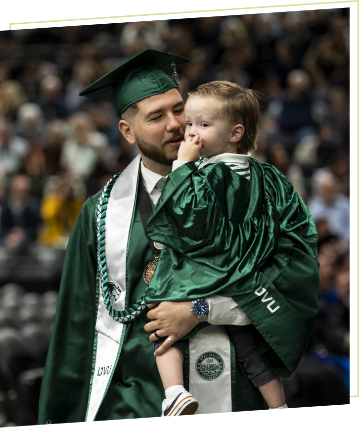 graduate student in cap and gown holding his son