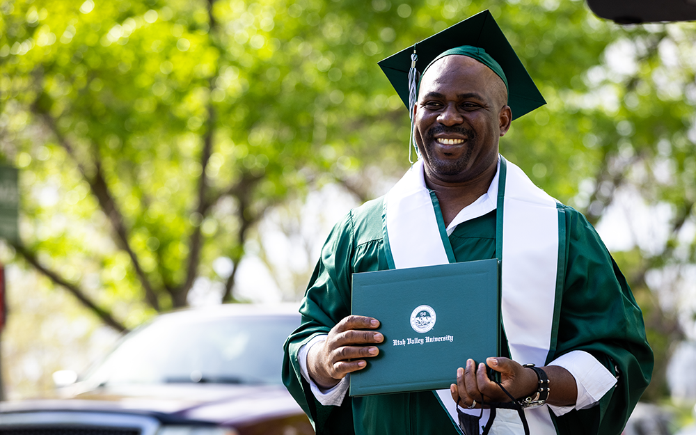 male graduate student in cap and gown holding diploma