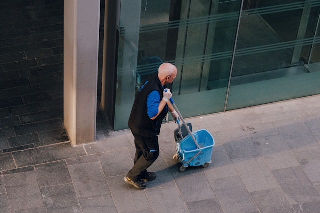 man pulls a cleaning cart near a building