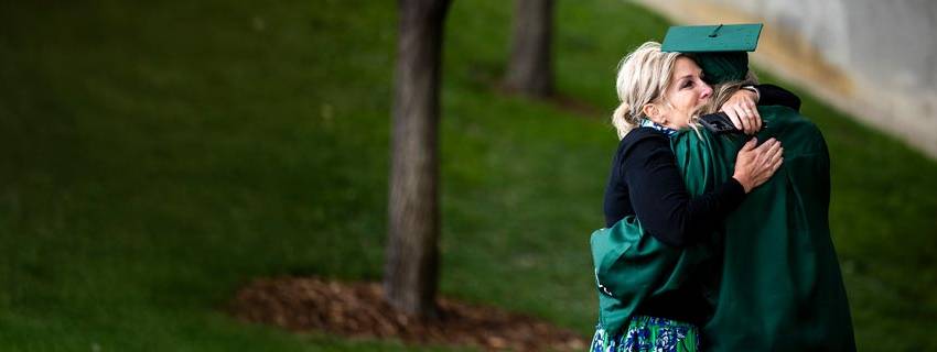 A woman hugging her son who is wearing UVU graduate attire.
