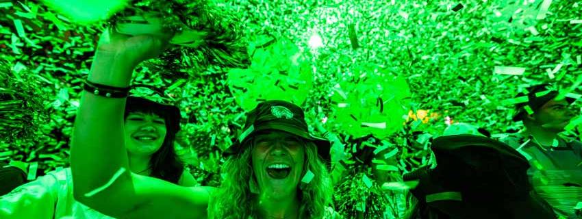 A group of people dancing while green confetti falls from the ceiling.