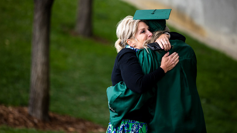 A mother hugging her child who is dressed in UVU graduate attire.