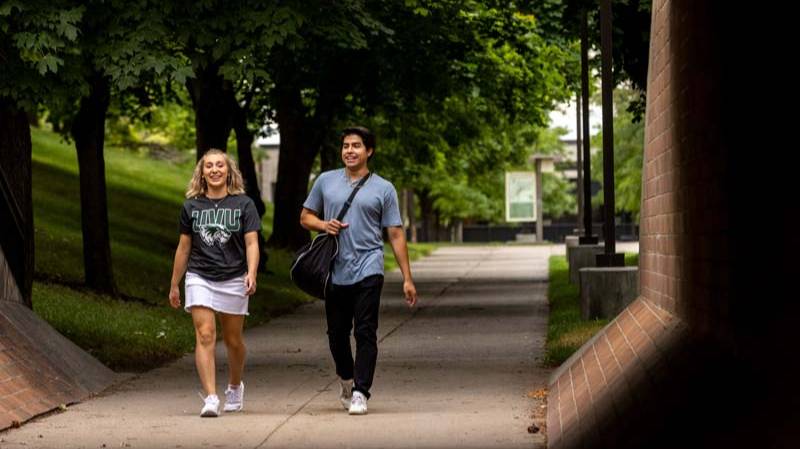 A man and a woman walking down one of the concrete walkways on UVUV's main campus.