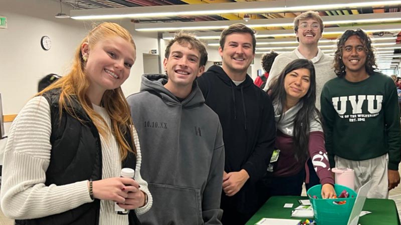 Students standing next to a table and smiling at the camera.