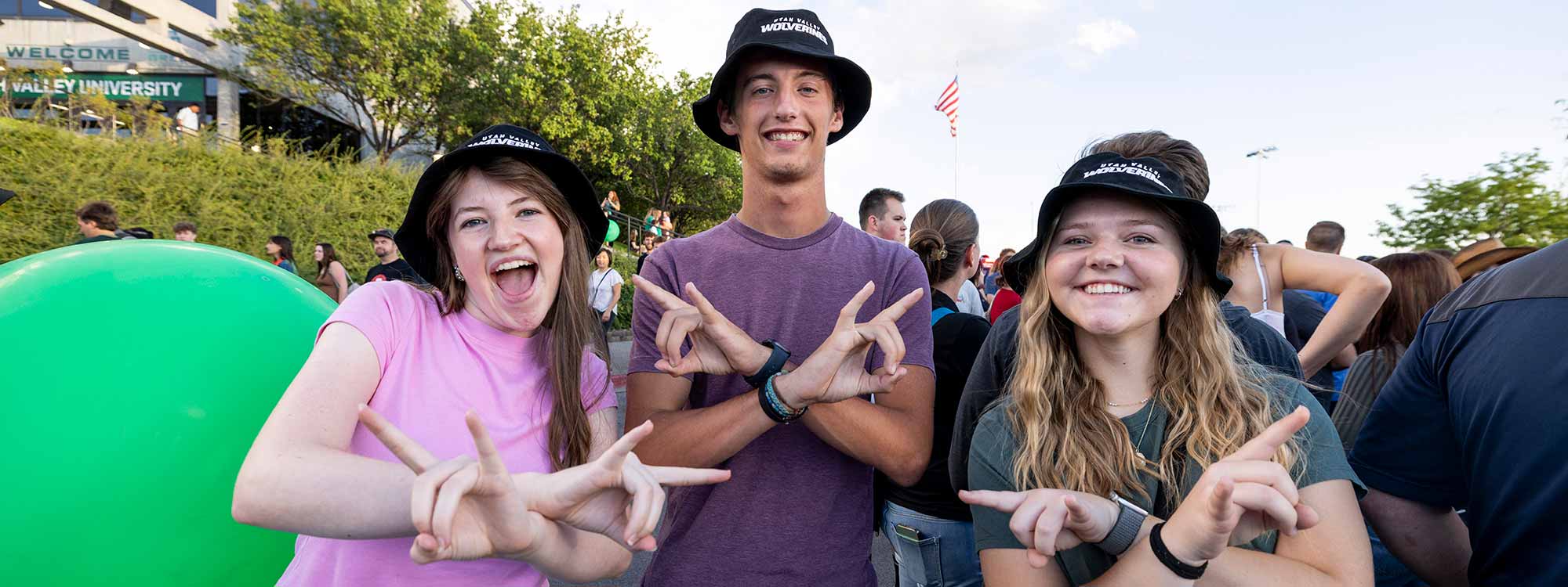 A man and two women standing next to each other and hold up the UVU hand sign.
