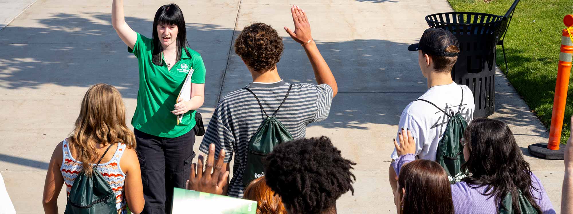 A group of new students follow a woman in a bright green shirt with her hand raised.