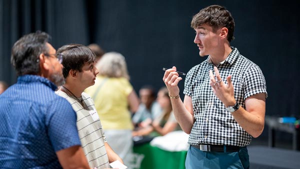 A man talking to a parent and student, he looks like as if he is explaining something to them.