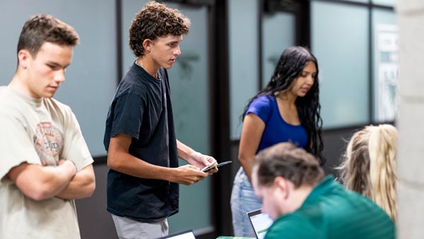 New UVU students standing in front of UVU staff who are gathering information from computers.