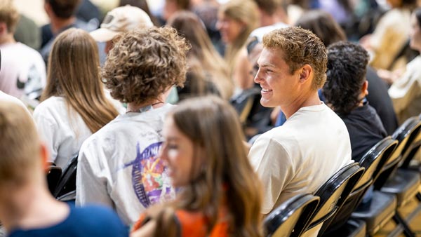 A large number of students sitting in an auditorium talking with each other.
