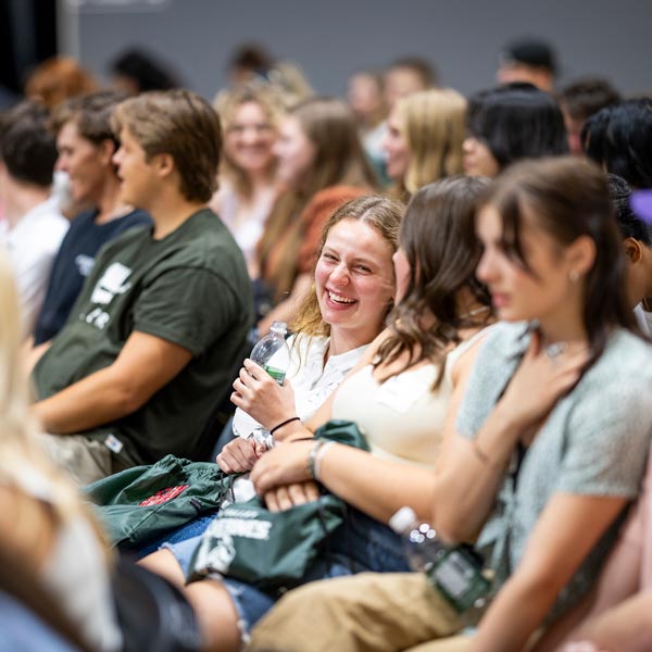 Students in an auditorium talking to each other and laughing.