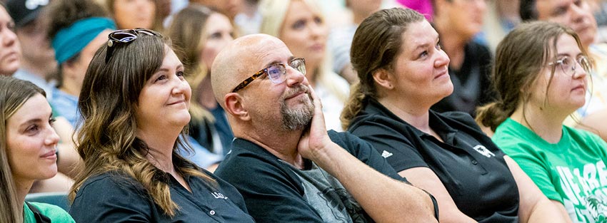 A woman and a man wearing UVU attire and holding up the Wolverine hand sign.