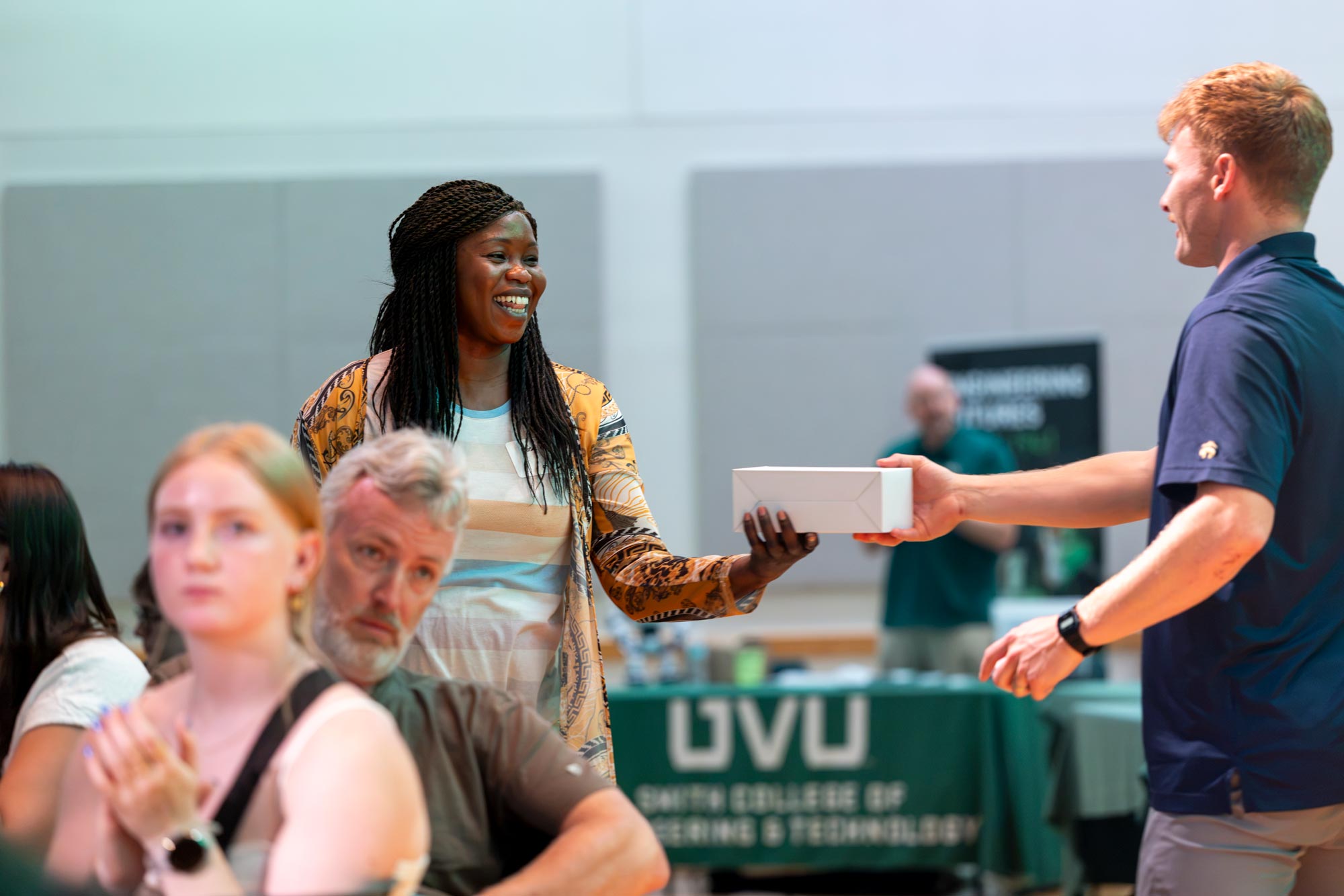 A woman accepting a reward that is in a box from a UVU employee.