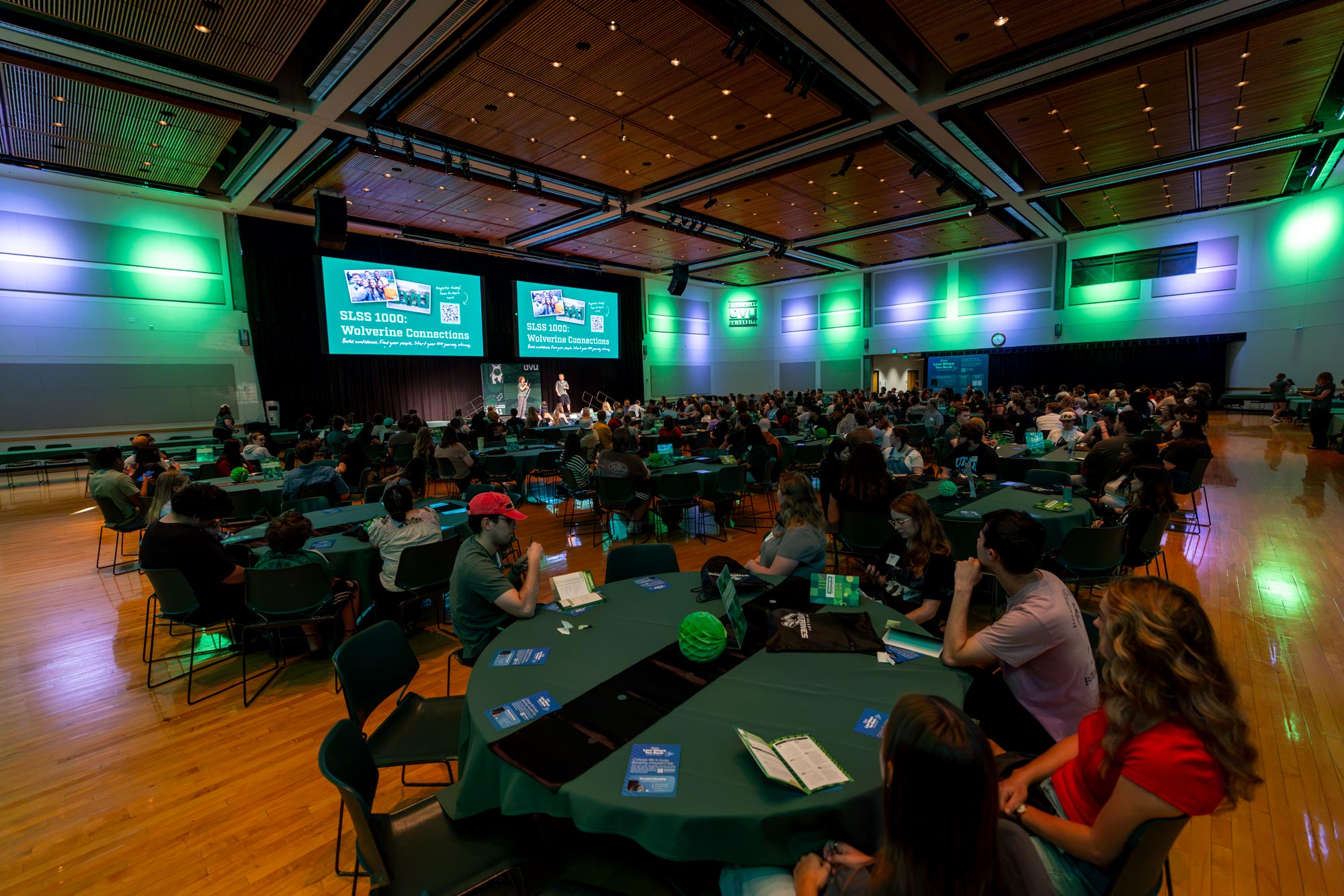 Students sitting in the UVU Ballroom looking at the jumbo screens with SLSS 1000 written on the screens.