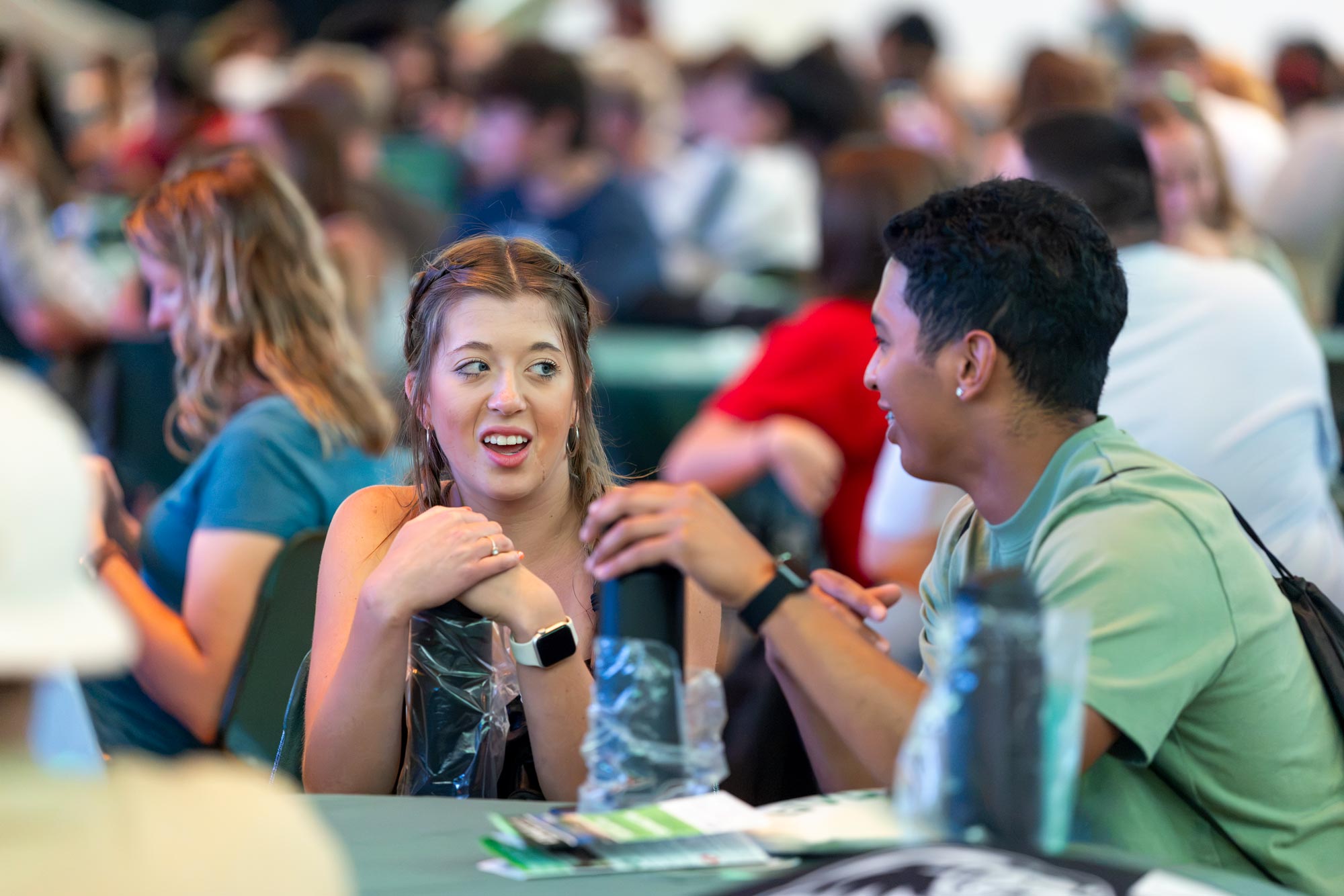 Two students sitting at table talking to each other.