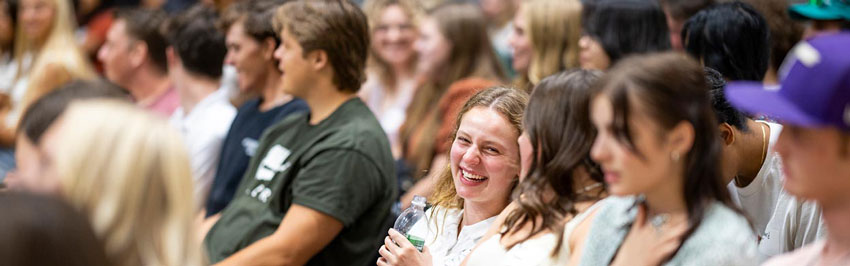 Students sitting in an auditorium, talking and laughing with each other.