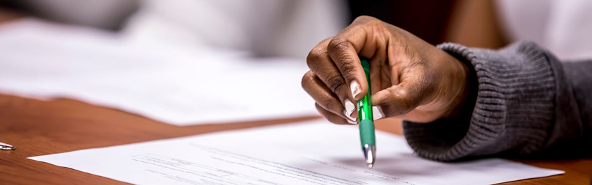 A hand holding a green pen on top of a paper.