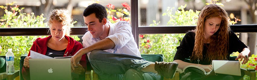 A man sitting inbetween two woman in front of a window. The man is pointing at the laptop screen of one of the woman.