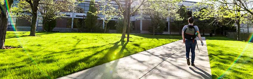 A student walking down a concrete path on UVU's main campus.