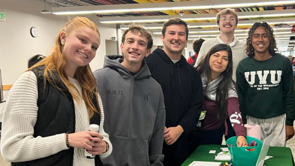 A group of students standing next to a table looking at the camera, smiling.