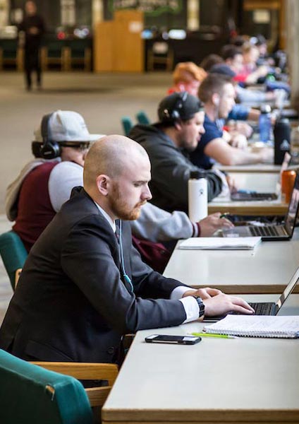 A man in a suit working on his laptop with a headphone in his left ear.