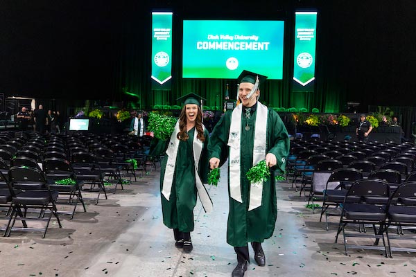 A woman and man in UVU graduate attire walking down the middle of the chairs at commencement once the ceremony is over.