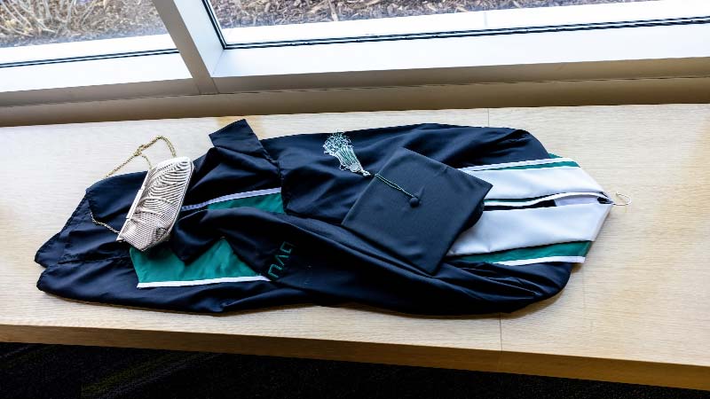 UVU cap, sashes, and gown laying on a wooden table in front of a window.