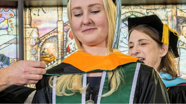 A UVU graduate having an orange sash put on them.