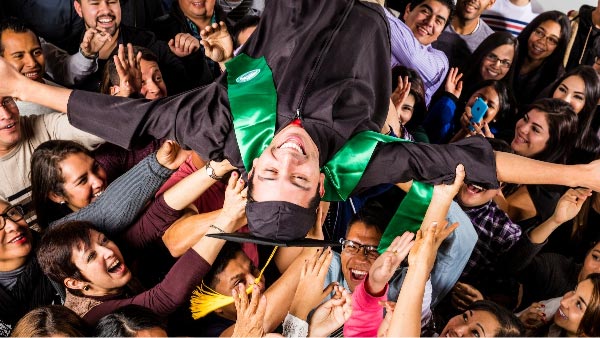 A man dressed in UVU graduate attire crowd surfing
