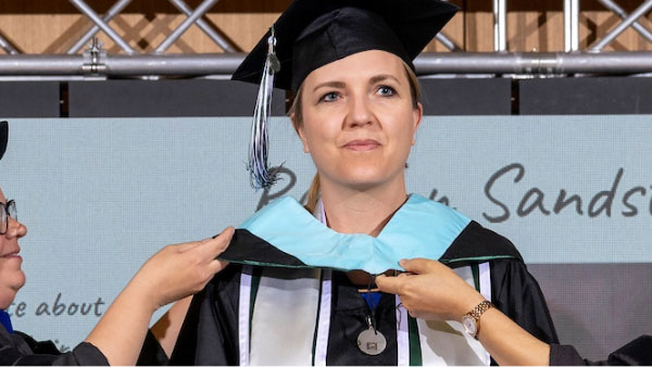 A UVU graduate having an light blue sash put on them.