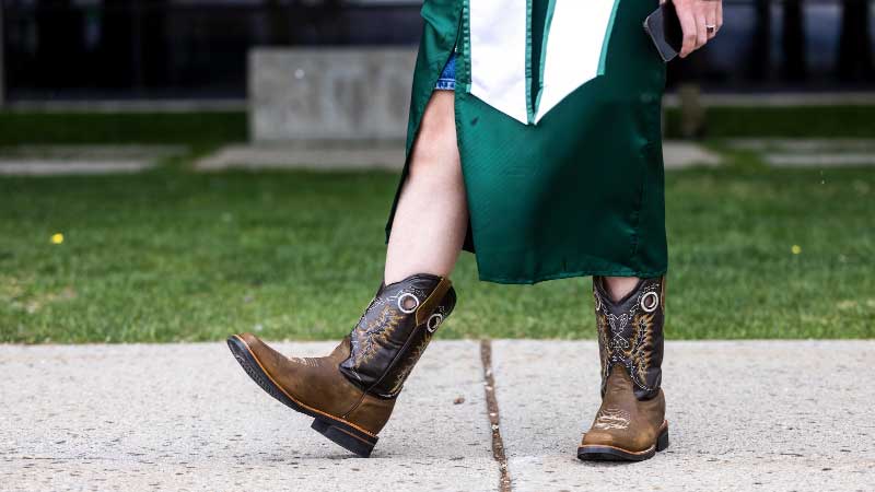 A UVU graduate wearing UVU graduation attire with cowboy boots.