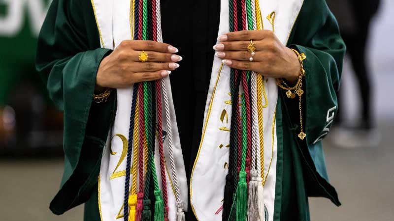 A UVU Graduate with Program Distinction Cords, in a variety of colors, draped around the back of their neck