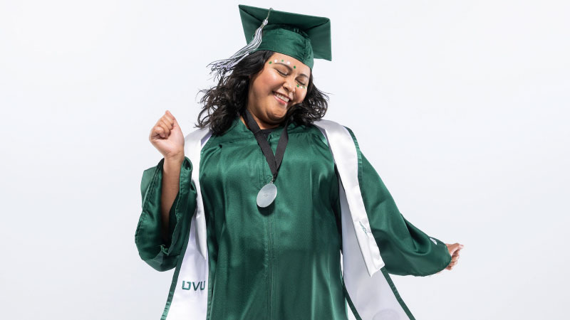 A woman dressed in UVU graduation attire, dancing.