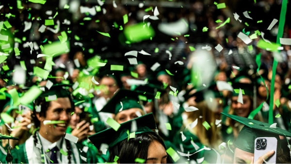 Graduates celebrating with green and white confetti falling around them.