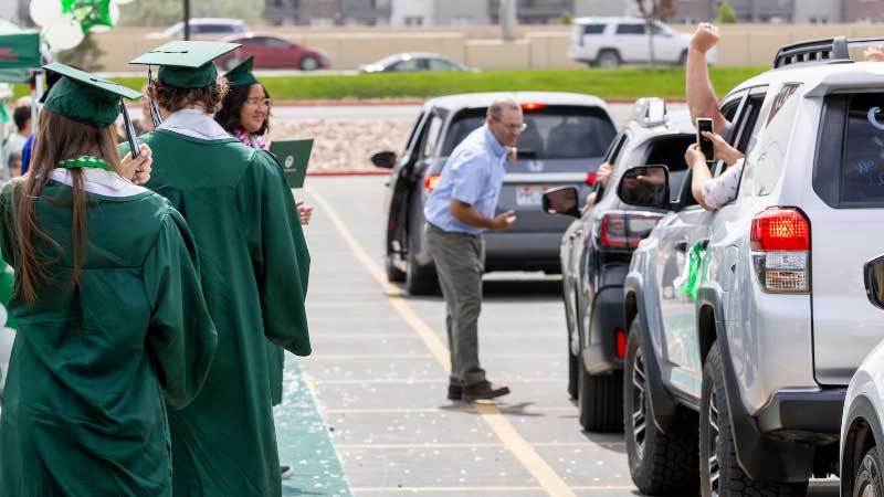 Parking Information Graduates in UVU attire on the left with a man directing cars on the right.