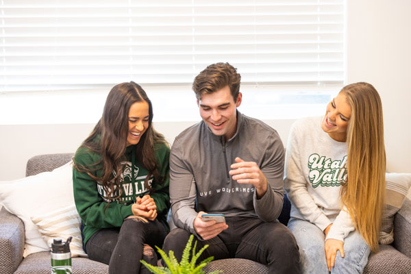 Three people sitting on a couch looking at one phone