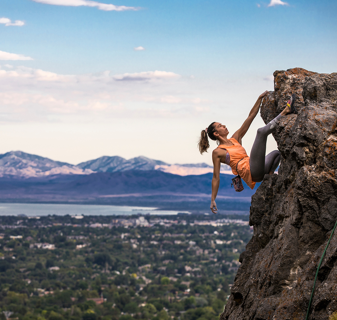 student climbing up a cliffside with a great view of the valley in the background