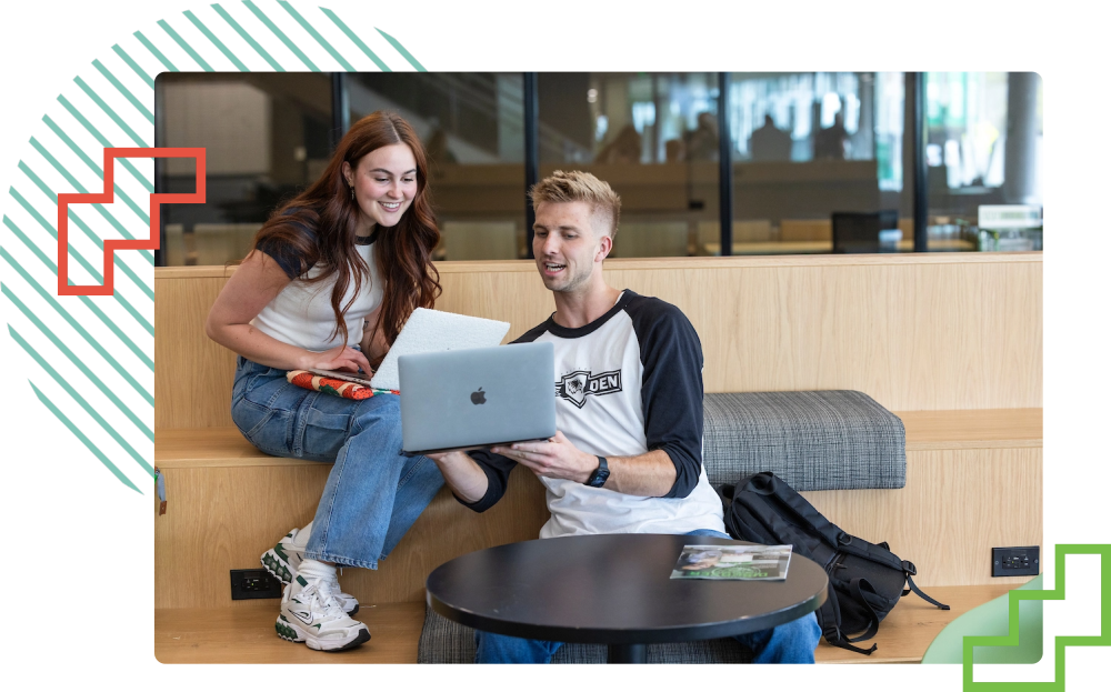 two students sitting at a table looking at a laptop