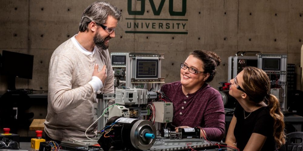 Professor helping two students work on machinery