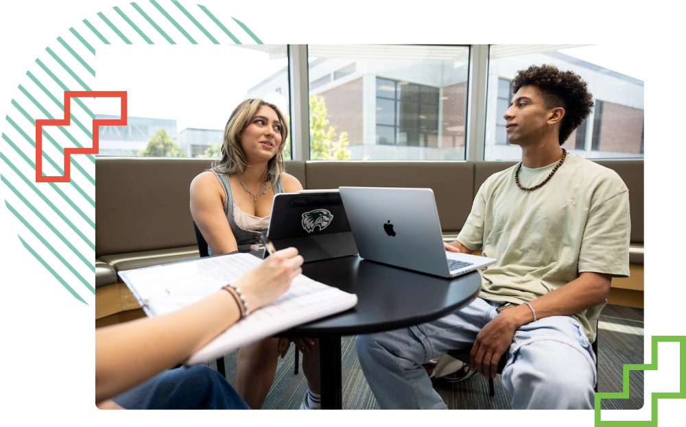 students seated around a table typing on their laptops