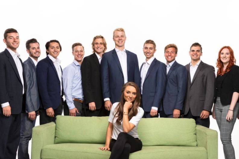 Group of students standing behind a green couch occupied by a female student