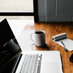 laptop on a table with a notebook and mug