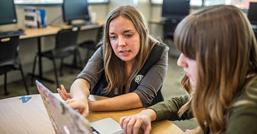 student assisting another student at a laptop