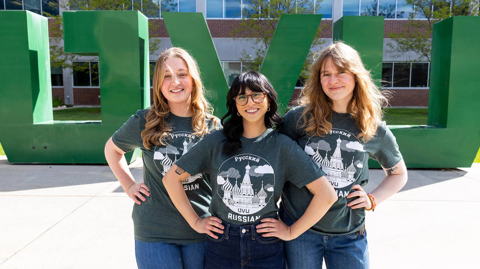 Three girls with Russian Studies T-shirts -n, standing in front of the big UVU letters outside