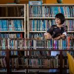 President Tuminez standing while looking at a bookshelf of books