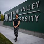 President Tuminez outside wearing a black blouse and skirt standing in front of UVU signage