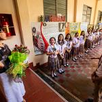 President Tuminez holding a bouquet of flowers while speaking to two lines of children