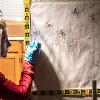 A woman looks on near a wall cover in splattered blood that has string coming out of it to show trajectory