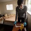 A man uses a specialized ruler to measure a dusty shoe print on a night stand