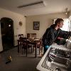 A man leans over a kitchen sink and uses a duster on the window to check for fingerprints